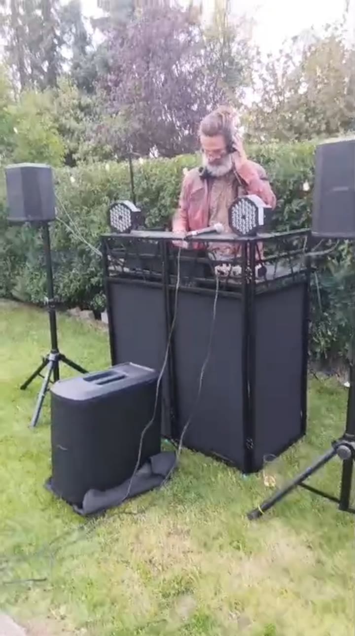 DJ mit Kopfhörern am Controller zwischen zwei Lautsprechern bei einer Gartensession