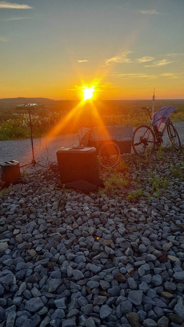 DJ-Controller, Lautsprecher, Fahrrad und Anhänger auf einer Halde bei Sonnenuntergang